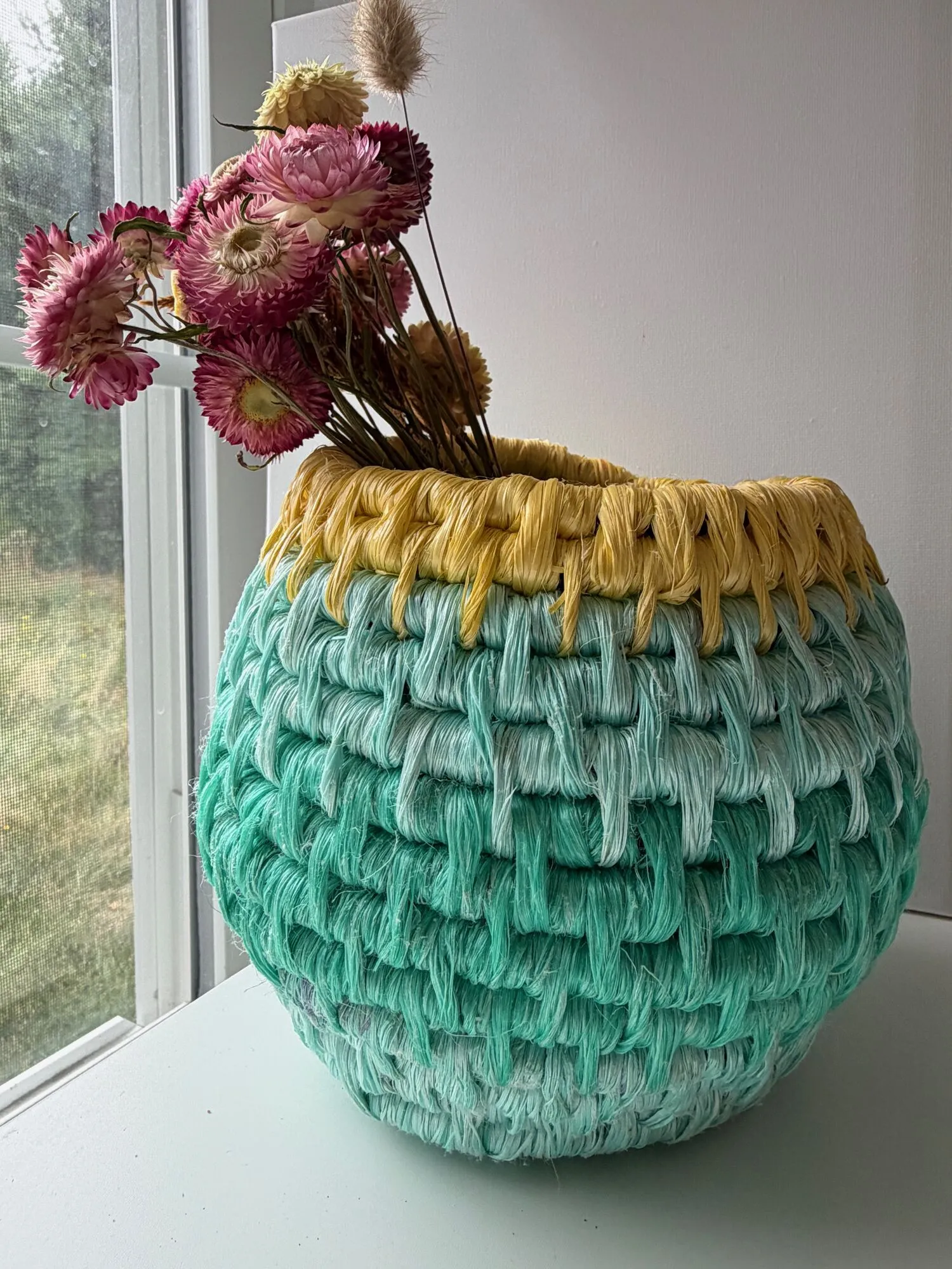 Aqua woven rope vessel with a yellow rim holding dried flowers