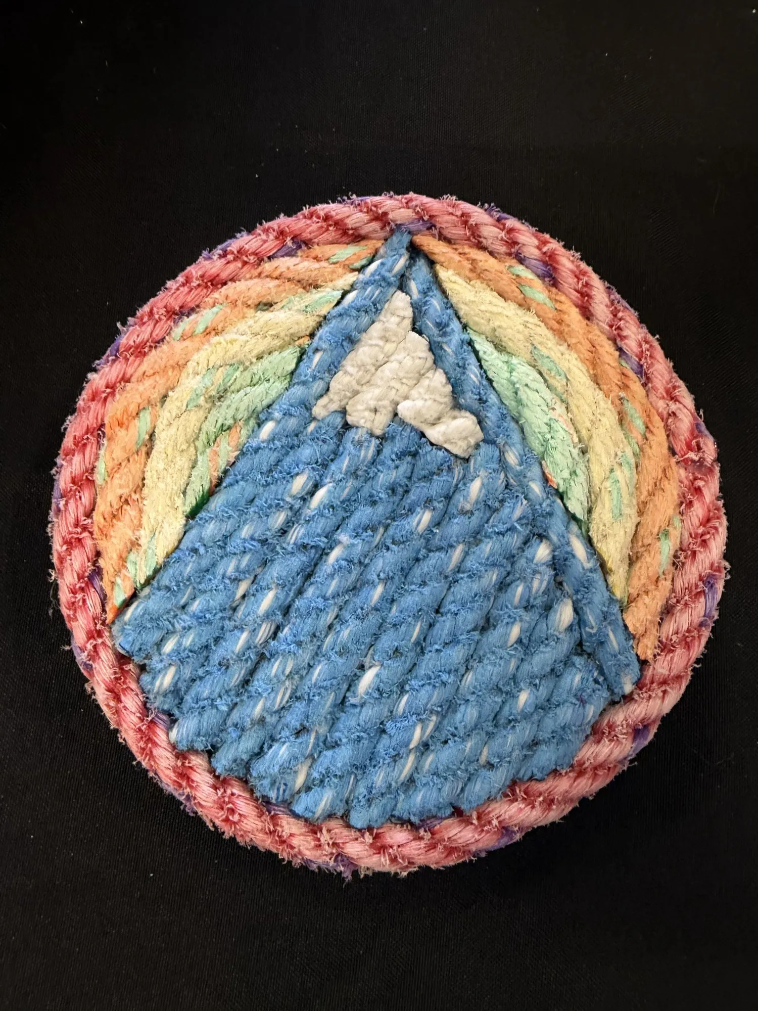Small round rope wall art of Sugarloaf mountain in blue against rainbow stripes, rimmed in coral