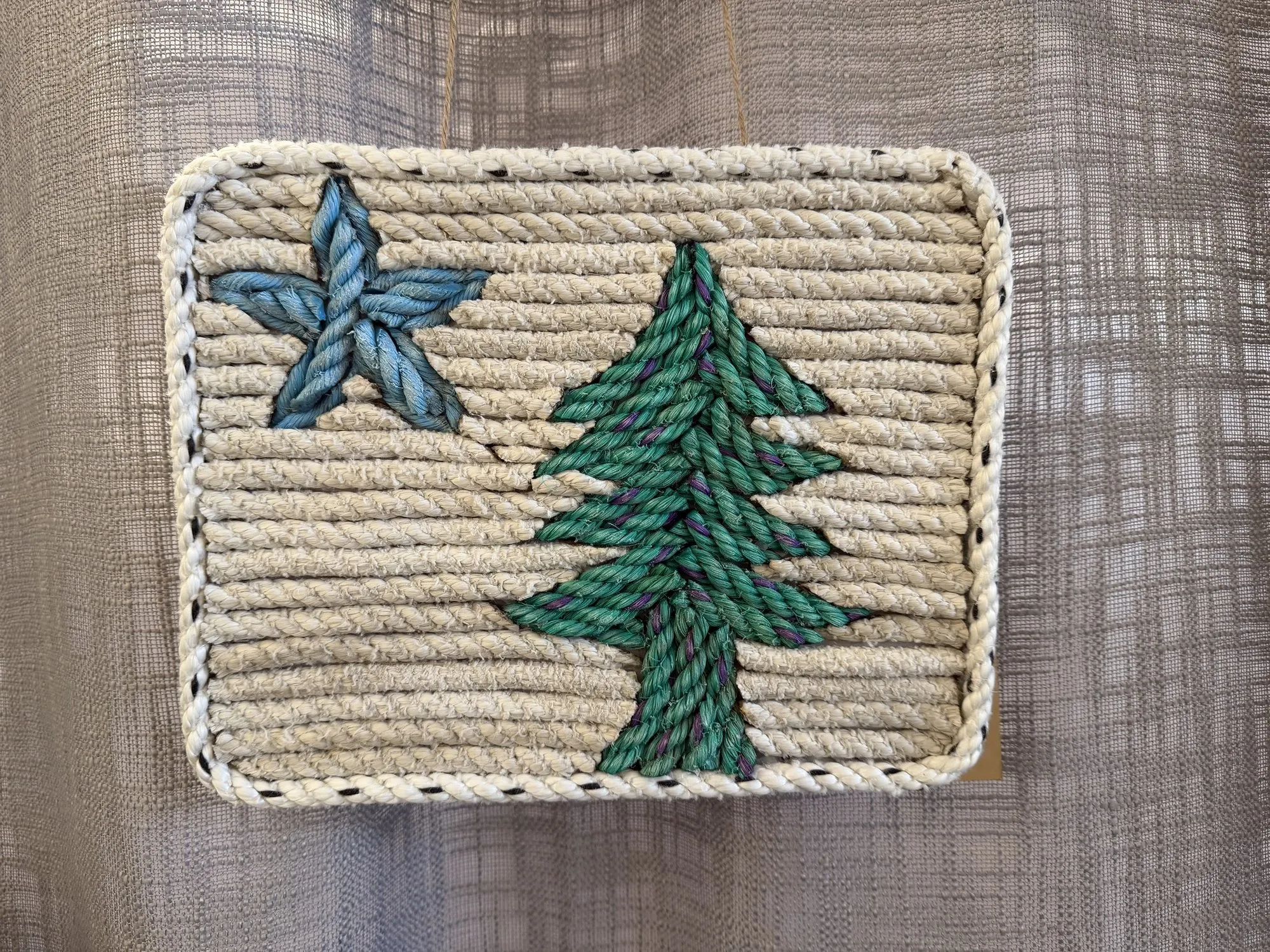 Rope wall art of a green pine tree and a blue star on a cream background