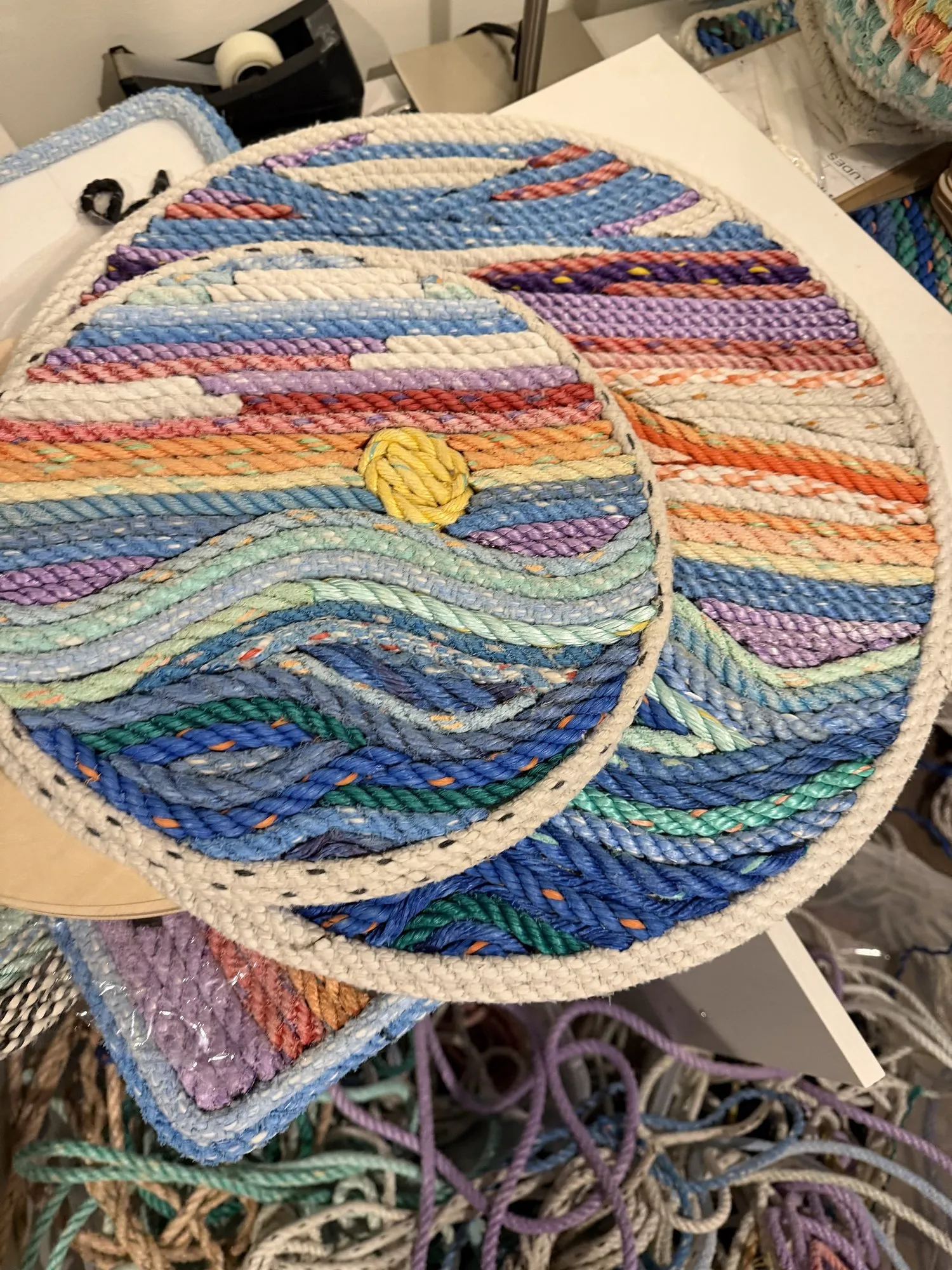 Small round rope wall art of a yellow sun setting over blue waves, resting on a larger sunset piece