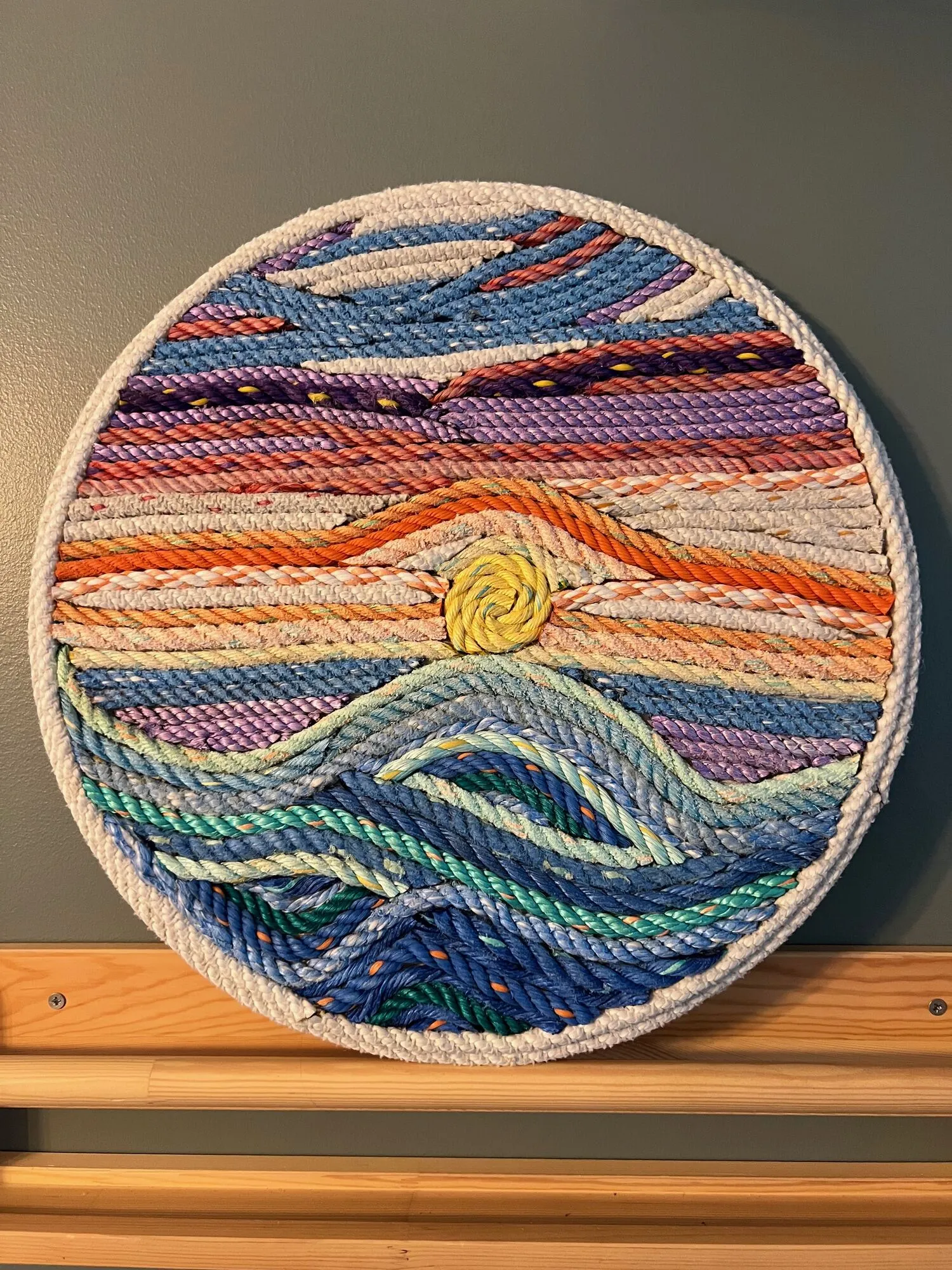 Round rope wall art of a sunset over ocean waves